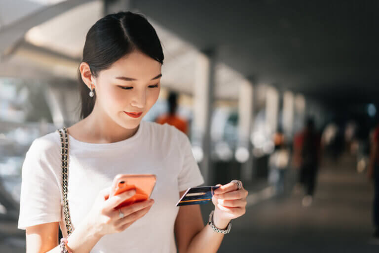 商务人士通过网上购物应用媒体概念. 快乐的微笑年轻的成年亚洲女性消费者使用信用卡和智能手机. City on day background with copy space.