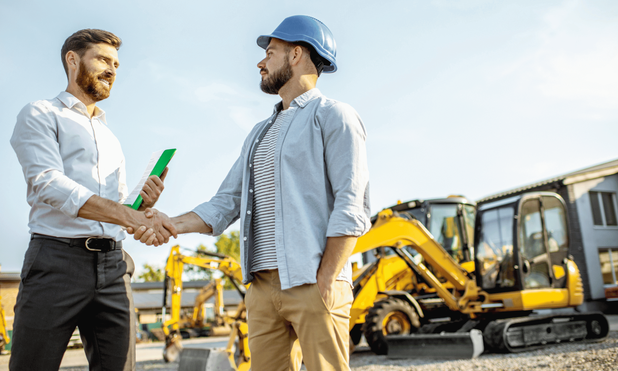 Two people standing around construction machines and shaking hand