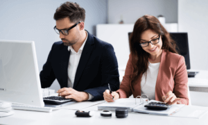 Two people. One with a computer and another with a calculator