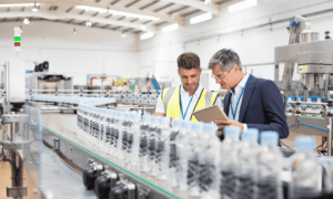 Two people looking at a tablet and inside a factory.