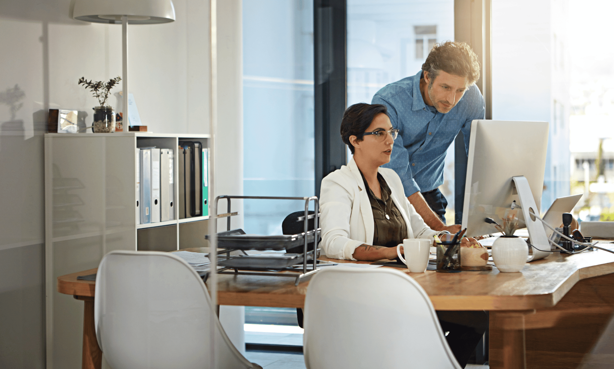 A person sitting at a desk and show another person something on a computer.