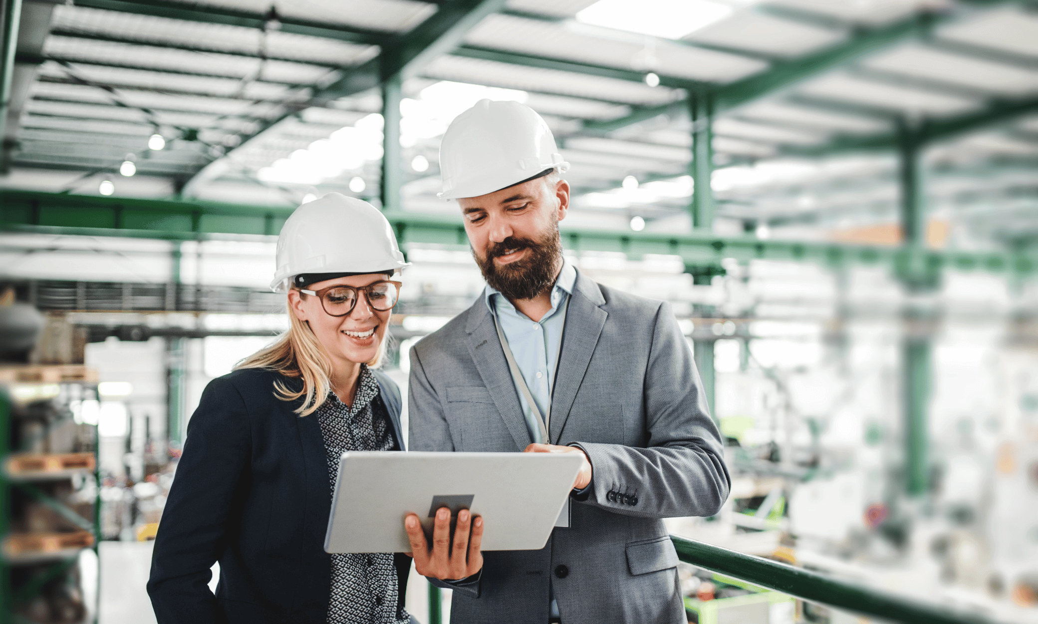 Two people wearing hard hats and looking at a tablet.