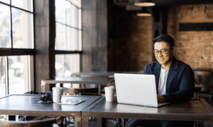 Someone sitting at a table and typing on a laptop.