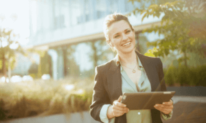 Someone smiling and holding a tablet outside.