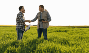 Two people stand in a field and shaking hands.