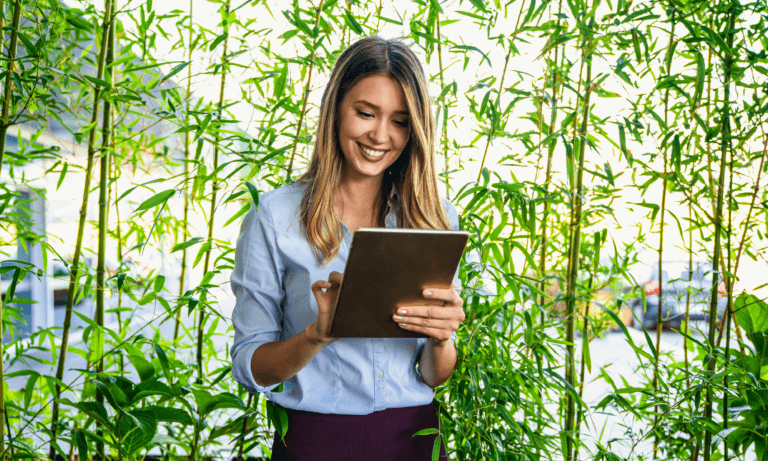 A person smiling at a tablet/iPad in an outdoor, nature-themed environment.