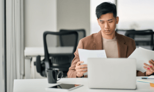 A person looking at a paper in front of their laptop.