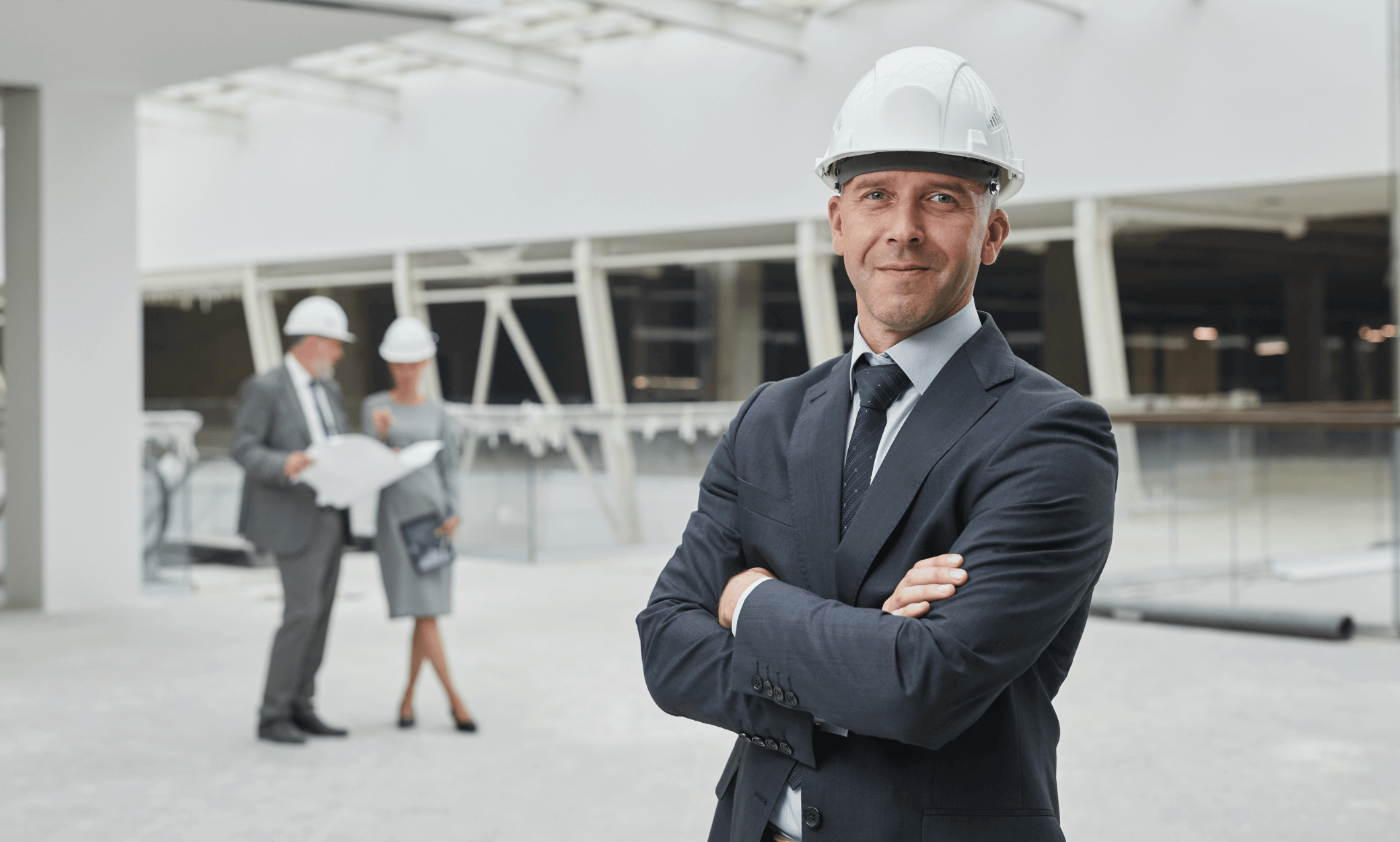 Construction worker smiling at the camera with two people discussing in the background.