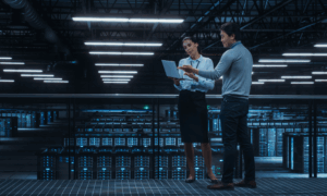 Two people discussing content on a laptop in a tech room.