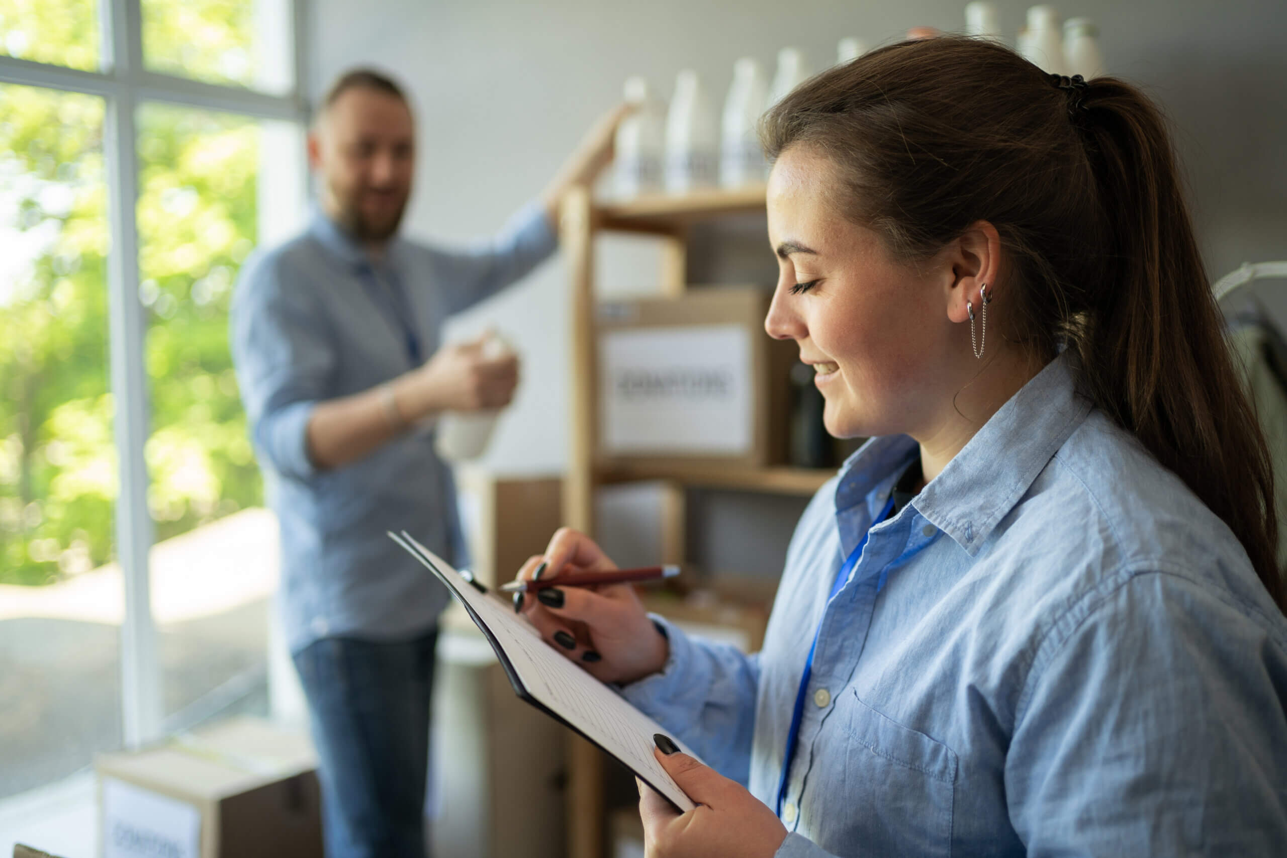 Female volunteer with clipboard and man taking box of food at refugee assistance center. Charity, donation and volunteering concept. Copy space