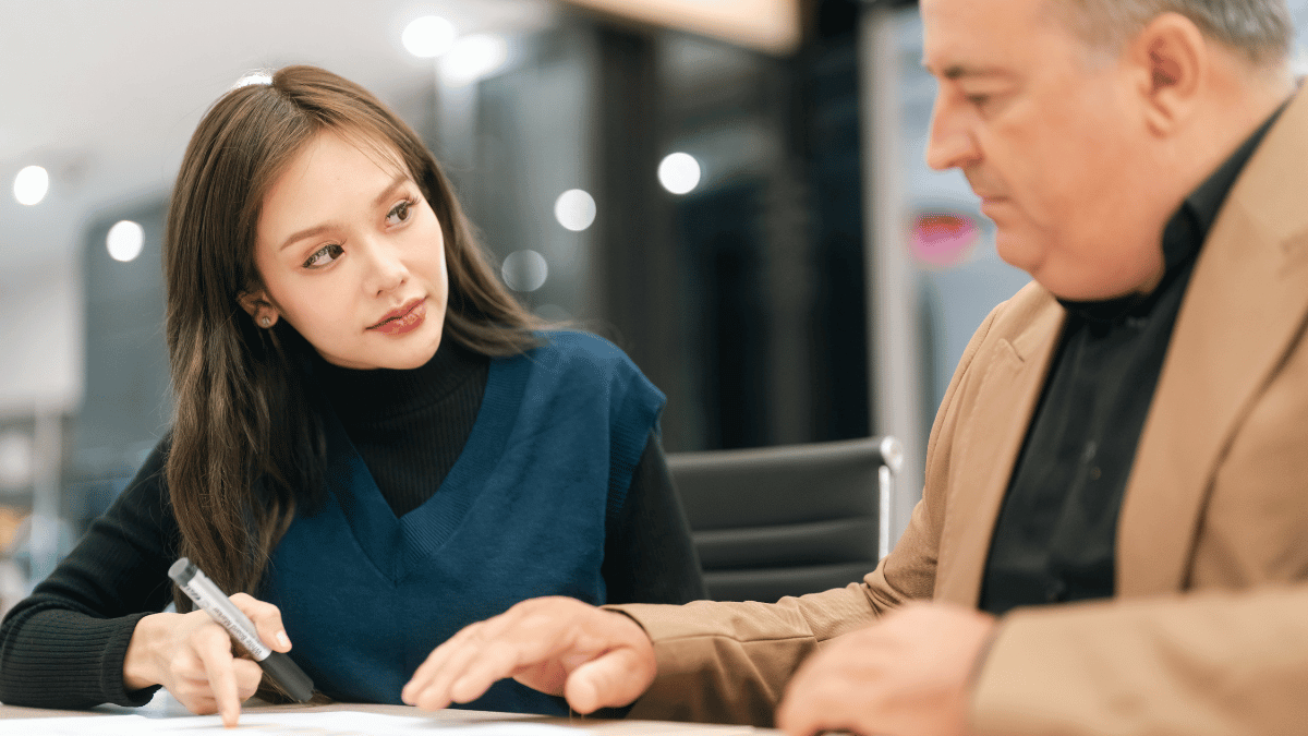 Business meeting young woman older man office table document review teamwork discussion consultation professional setting indoor scene